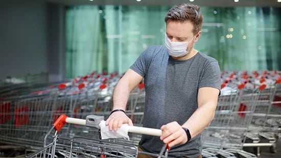 Grocery shopper wearing face mask, wiping cart handle with anti bacterial wipe.