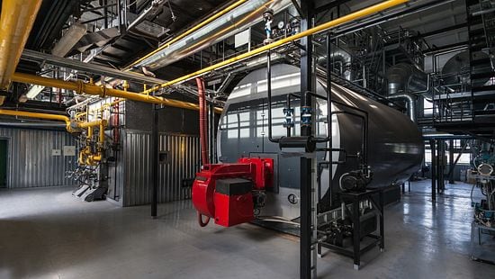 A boiler in a large and clean boiler room.
