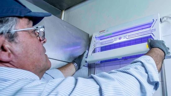 Technician installing a wall-mounted UV insect light in a food preparation area.